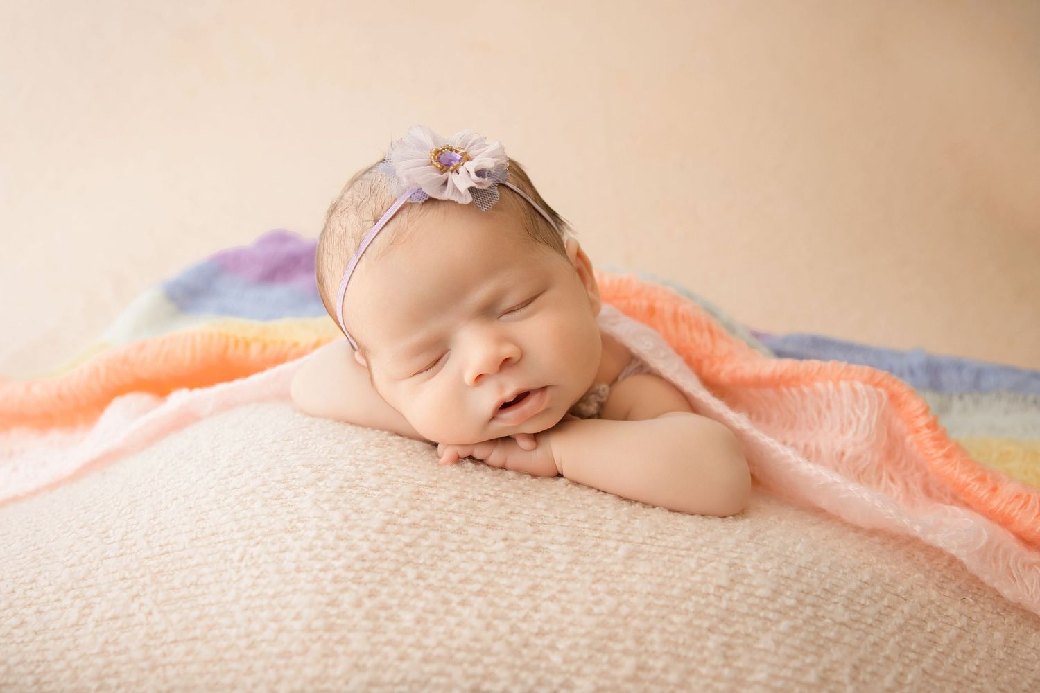 Delicate newborn photography with soft peach tones and textured blanket details.