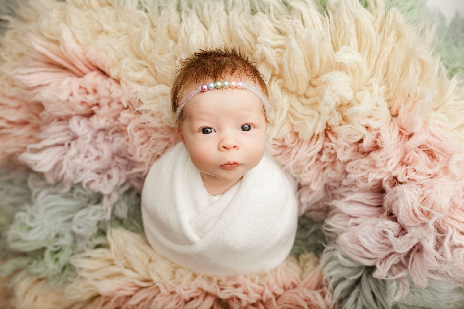 A baby wearing a white wrap lies on a soft pink and gray tulle backdrop in a newborn photography session.