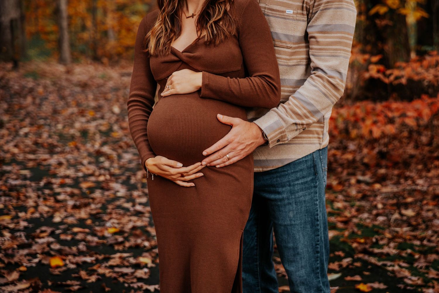 A maternity photo shoot in a park during autumn with fallen leaves covering the ground.