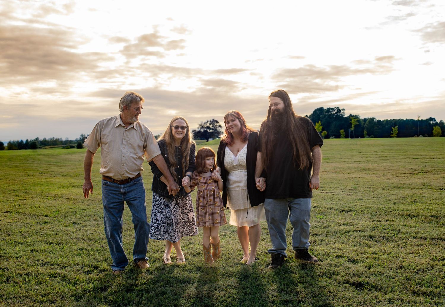 A group walks together across a scenic grassy field at sunset with warm golden light in the background.
