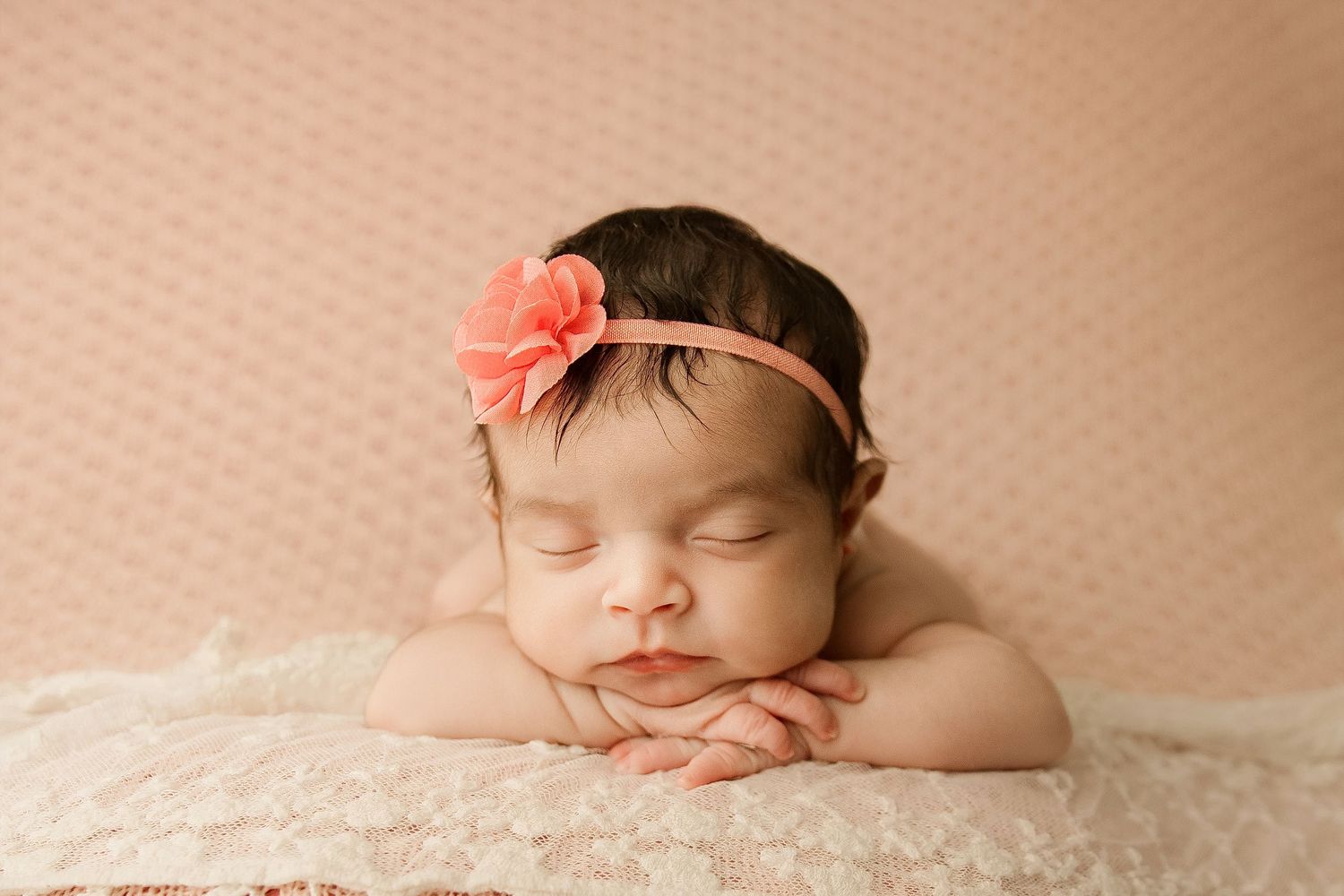Artistic newborn portraits with peach floral headband against neutral background.