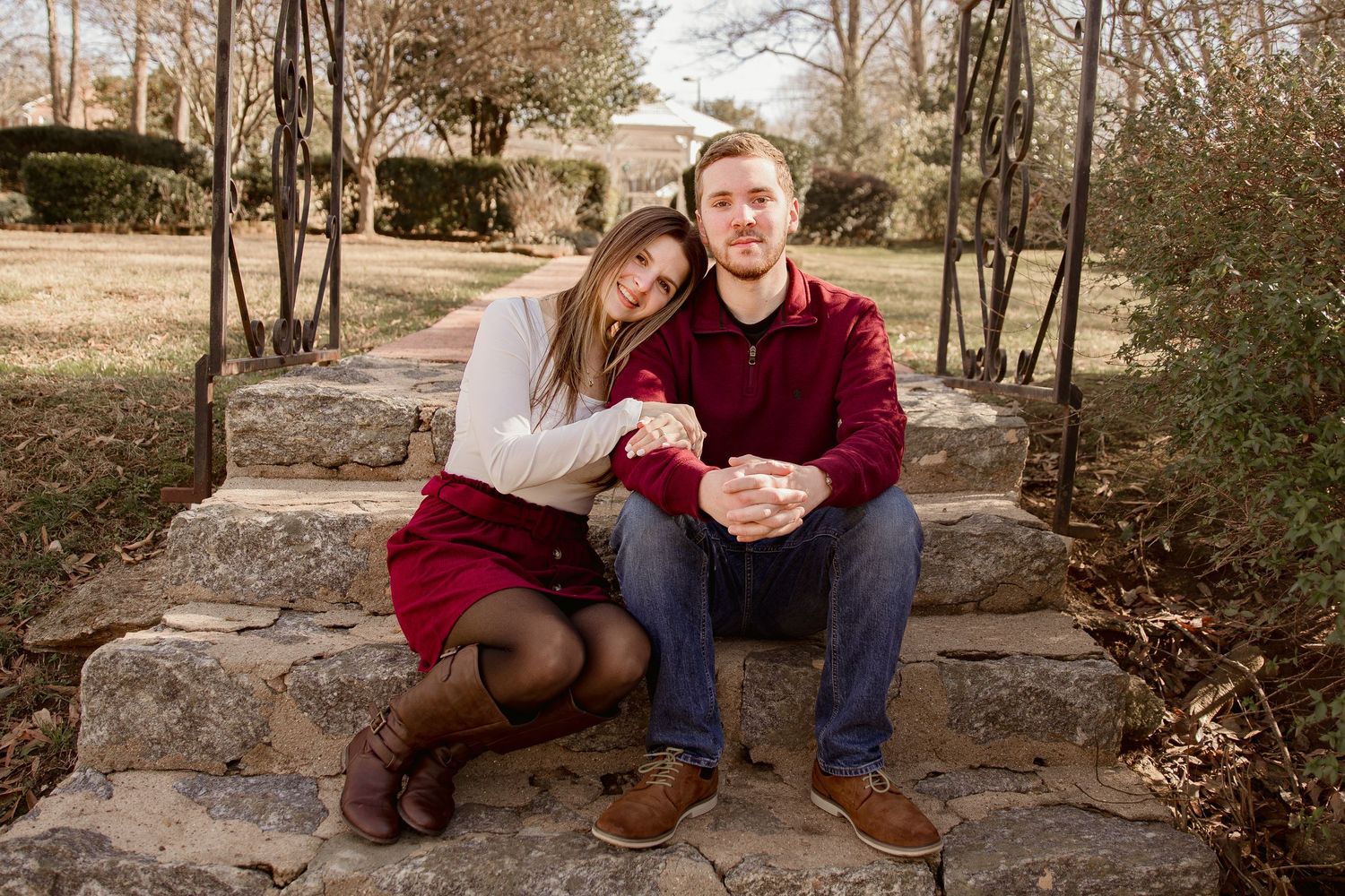 A couple sits together on stone steps in an outdoor autumn setting wearing coordinated burgundy and blue outfits.