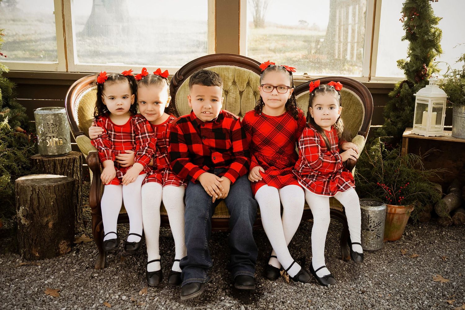 A group sits together on a wooden bench wearing coordinated red and black buffalo plaid outfits for a holiday photo.