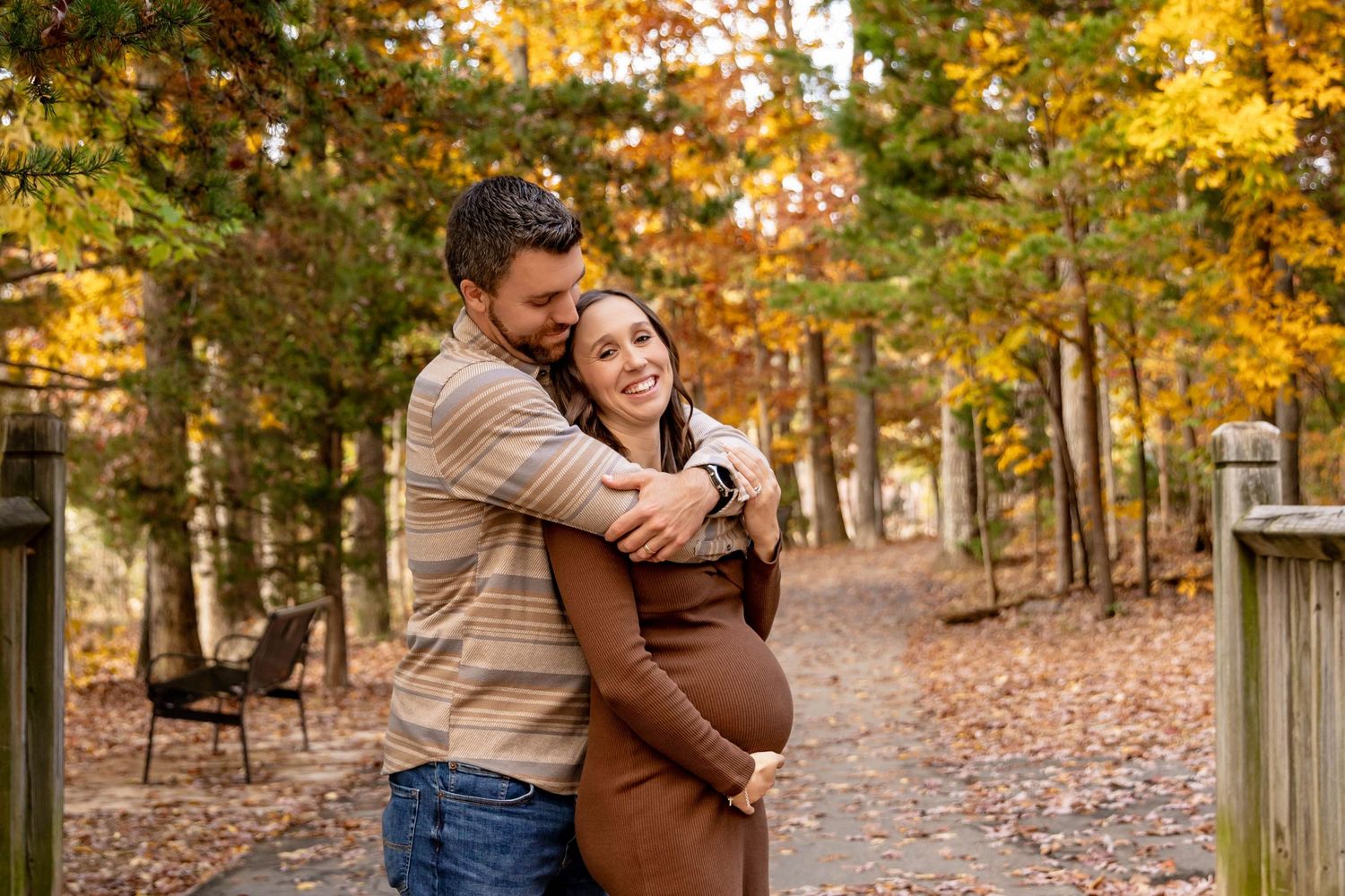 A couple embraces in a sun-drenched autumn forest with golden leaves scattered on the ground.