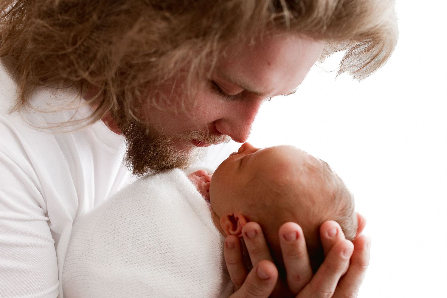 A tender moment captured as someone leans in close to a sleeping baby wrapped in white fabric.