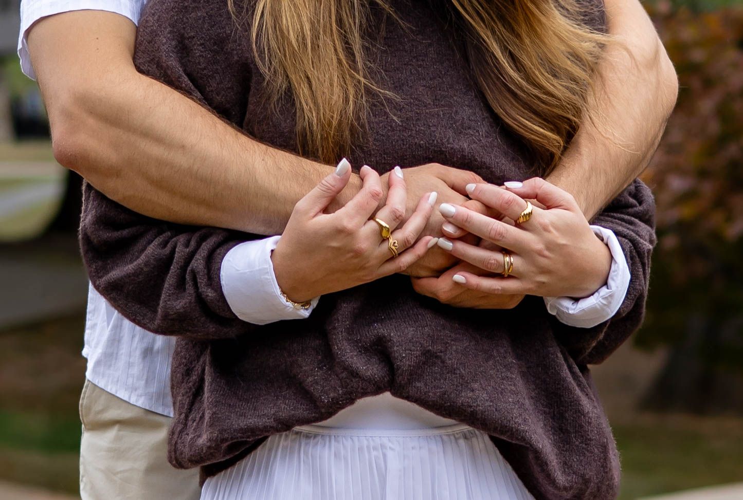 Close-up shot of hands holding each other tenderly against a blurred outdoor background.