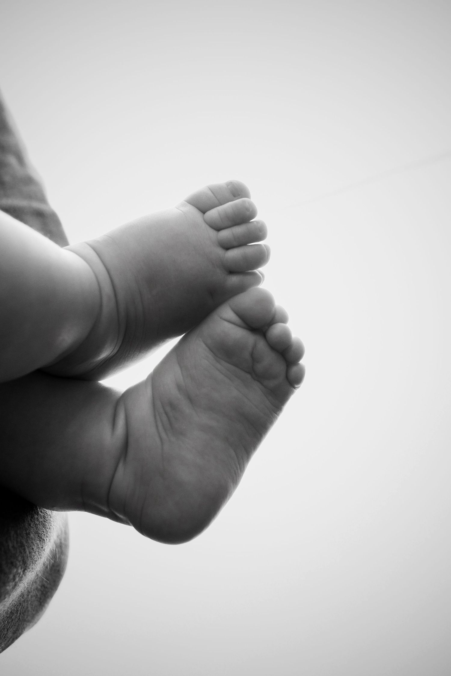Black and white close-up of a newborn baby's tiny bare feet and toes against a soft, light background.