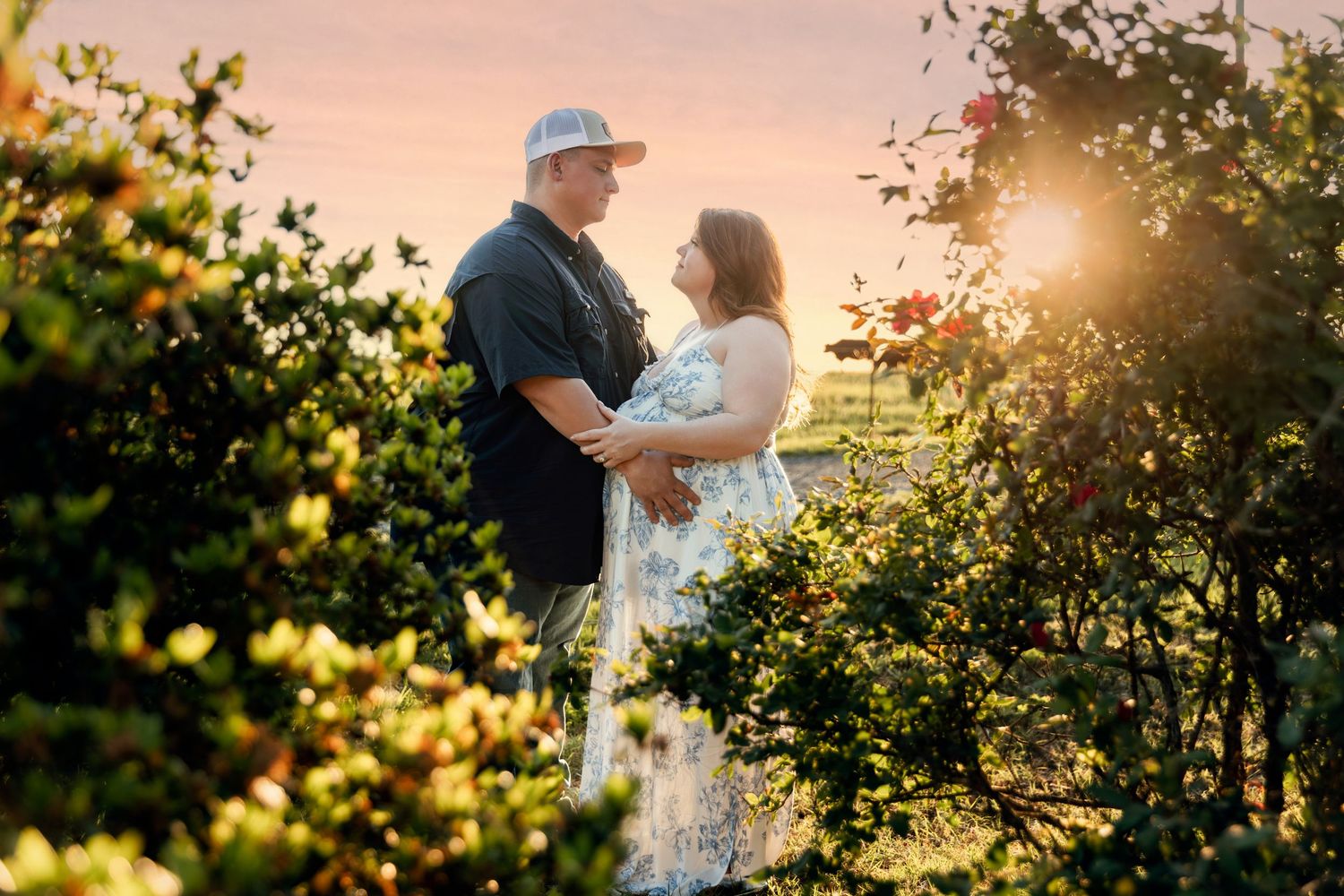 Couple embracing in a lush garden at golden sunset, surrounded by colorful blooming roses and shrubs.