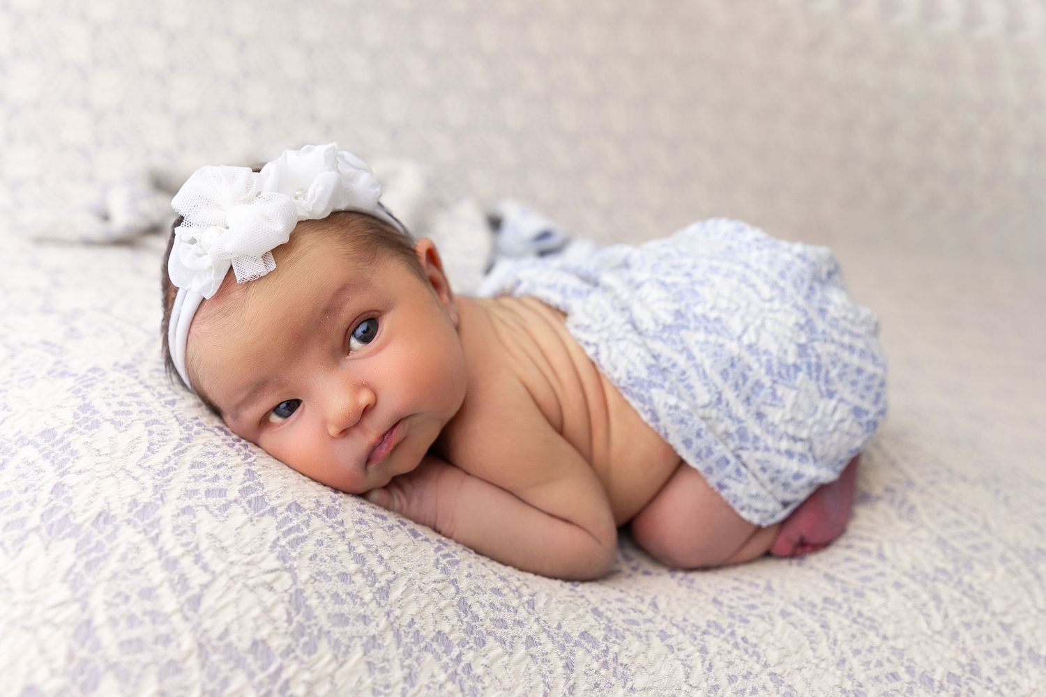 A newborn baby wearing a white cap lies on soft white bedding in a series of gentle sleeping poses.