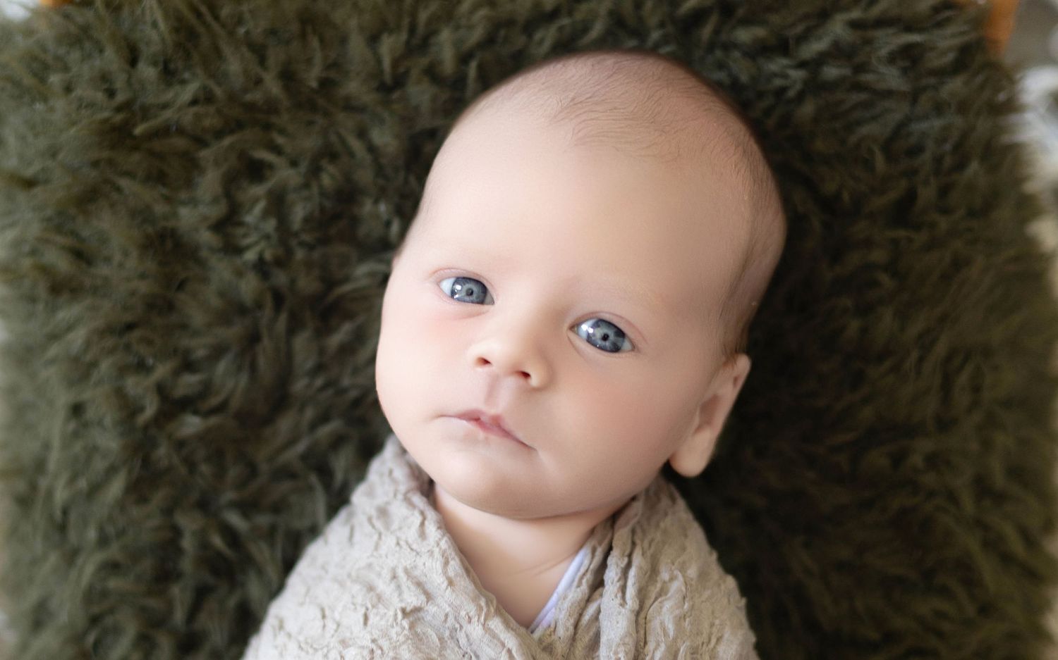 A baby wearing a white lace dress sits against a dark green textured background.