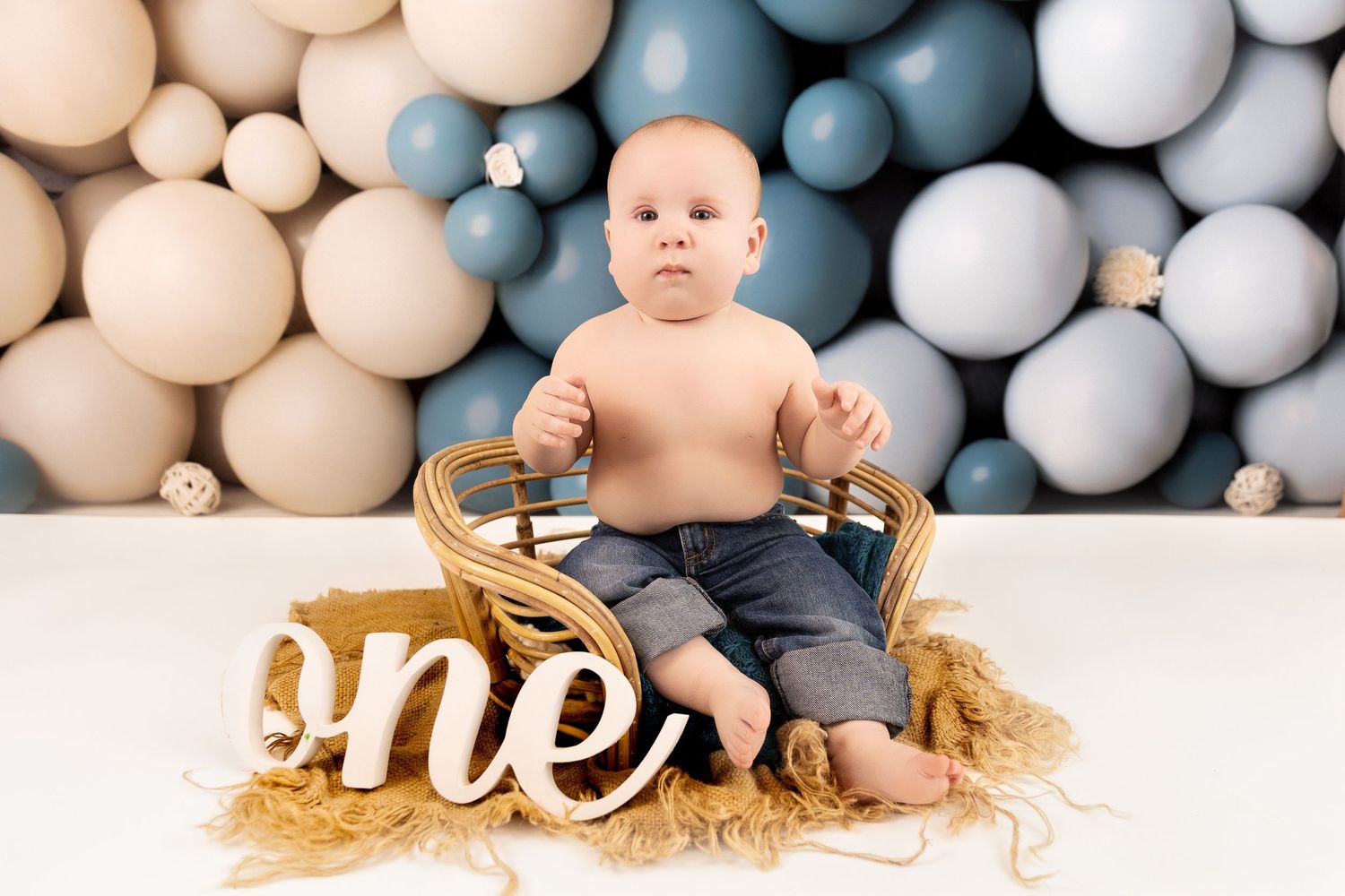 A festive first birthday cake smash photo session setup with blue and white balloons and golden decorative elements.