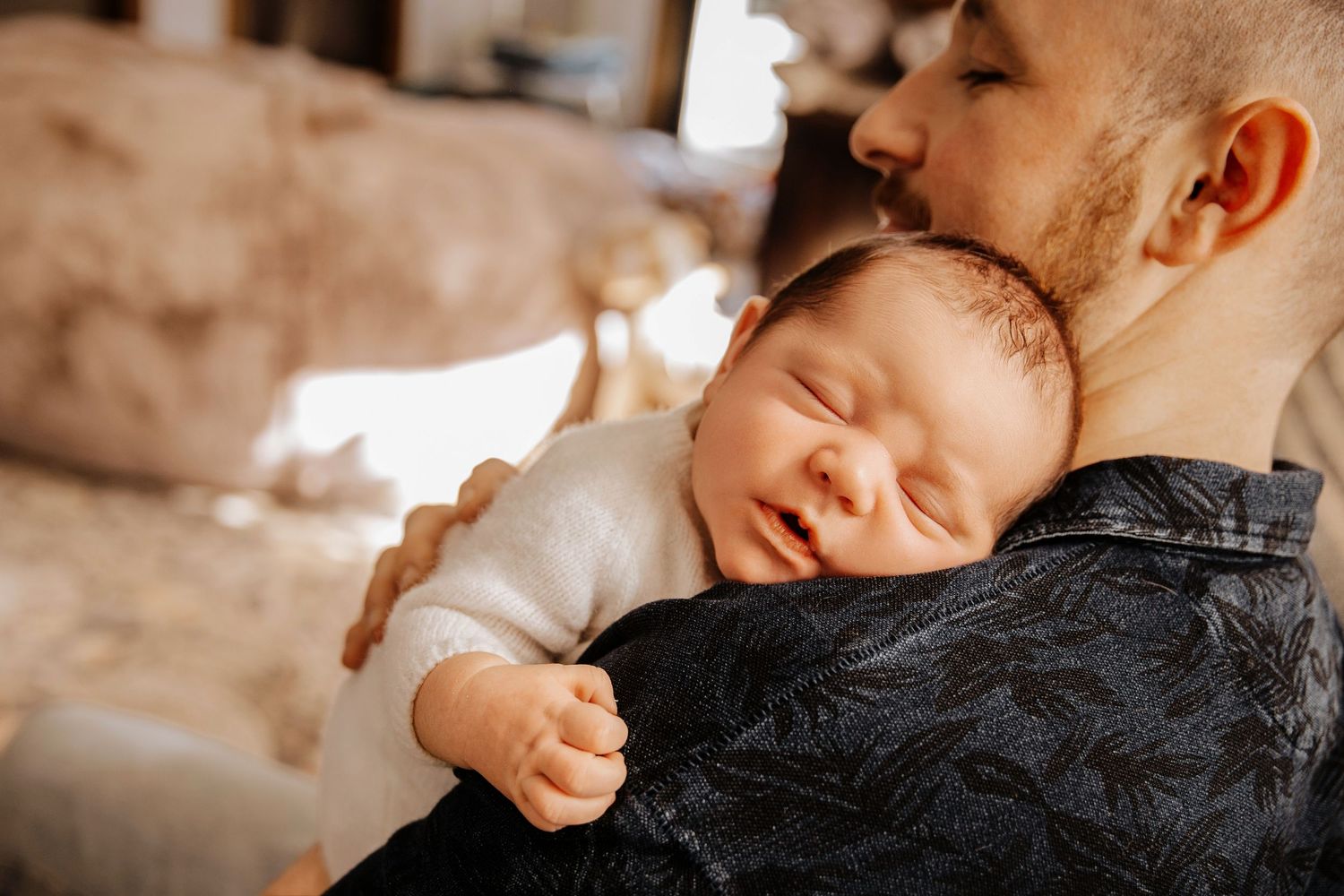 A sleeping baby rests peacefully on someone's shoulder in a warm sepia-toned photograph.