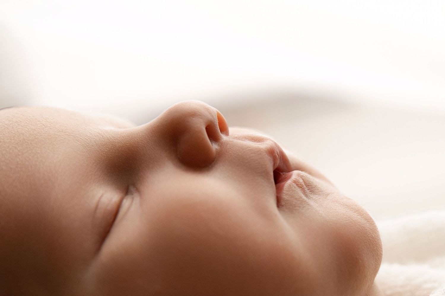 Close-up of a sleeping newborn baby with soft skin and peaceful expression on a white blanket.