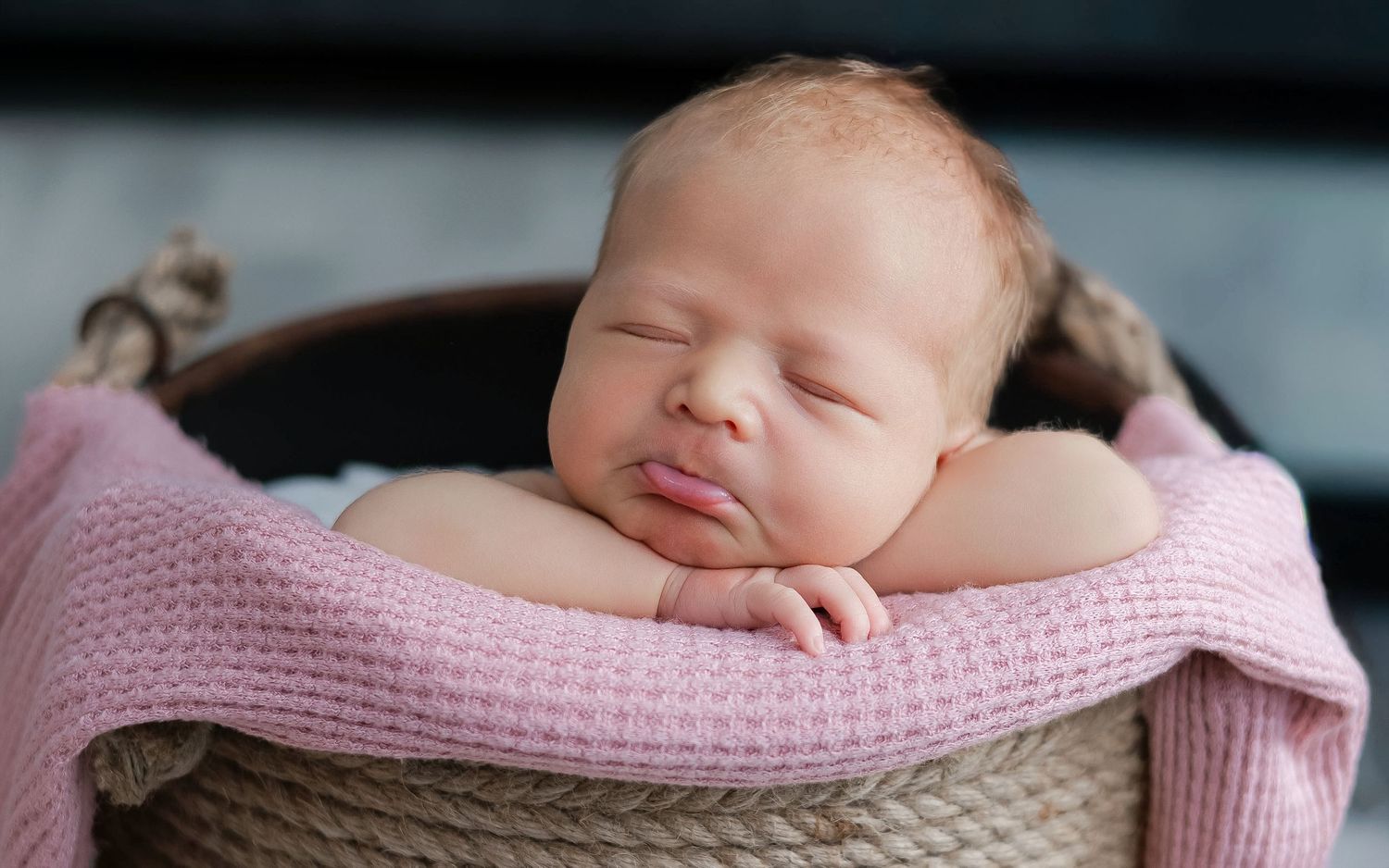 A sleeping newborn baby swaddled in soft pink and beige blankets rests peacefully during a professional photo session.