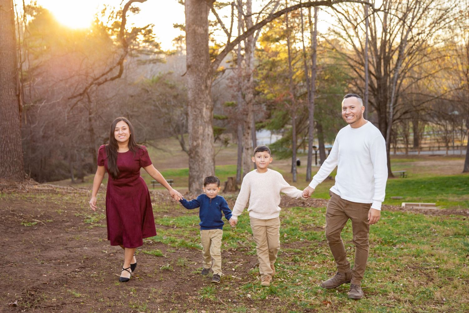 A family walks hand in hand through a park at sunset with golden sunlight filtering through autumn trees.