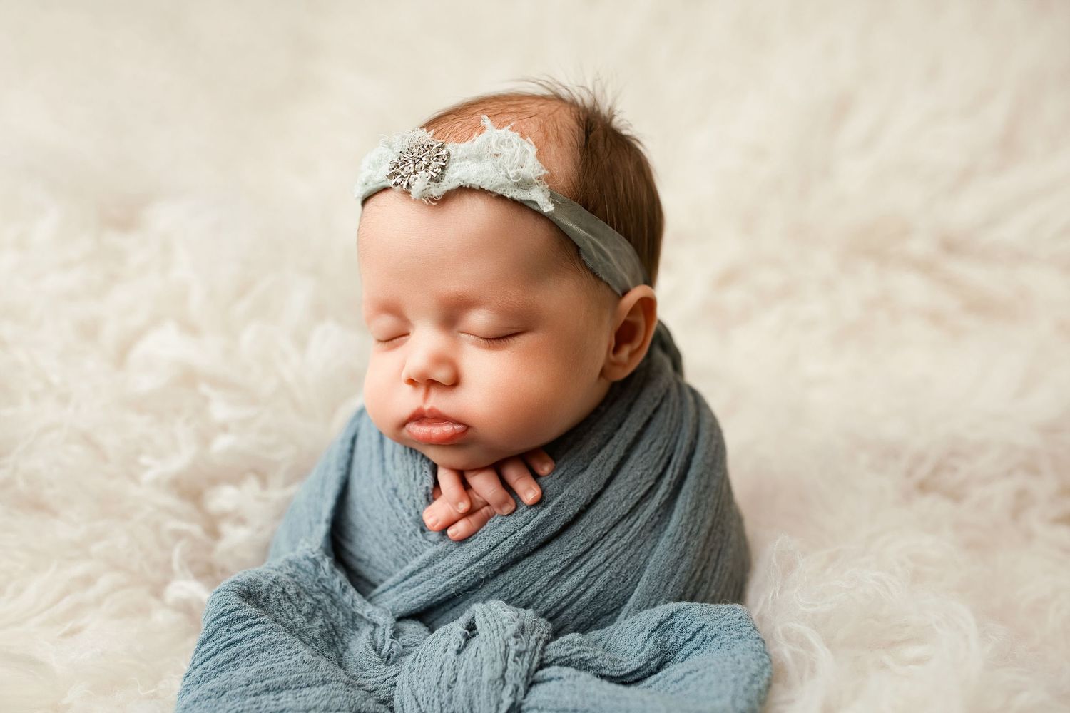 A newborn baby wearing a gray knit outfit sleeps peacefully on a textured cream-colored blanket.