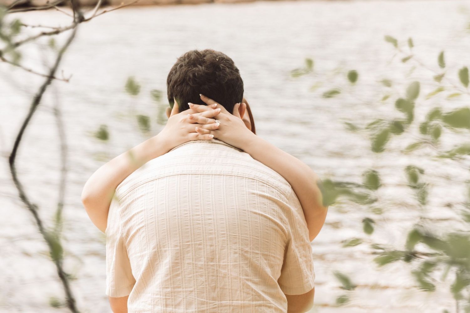 Man sitting alone by a tranquil lake, head in hands, surrounded by lush green trees in a peaceful outdoor setting.