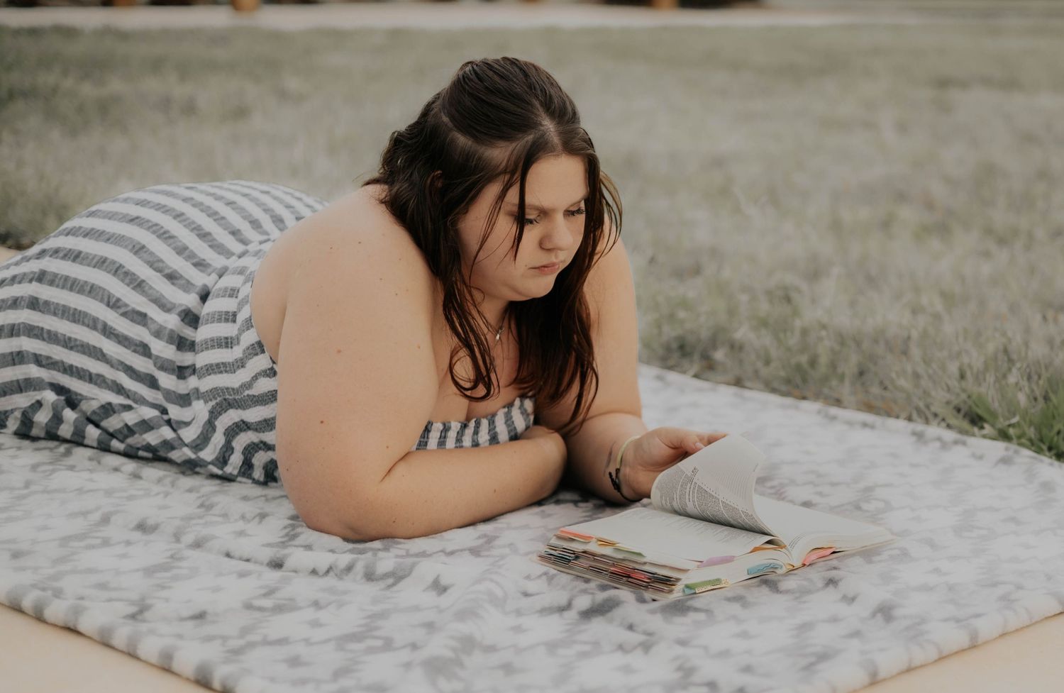 A person lies on a white blanket outdoors while reading a book on a sunny day.