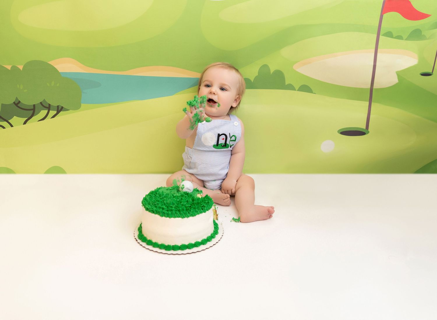 A series of milestone photos showing a baby's first year growth next to a green birthday cake with number one candle.