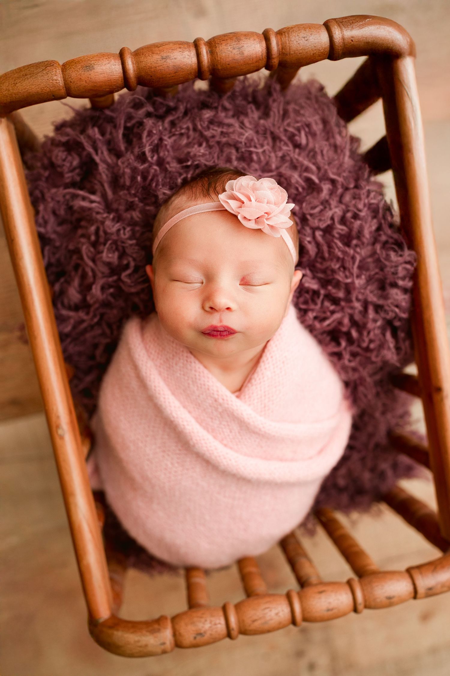 A series of images showing a sleeping newborn swaddled in pink with dark curly hair against a wooden backdrop.