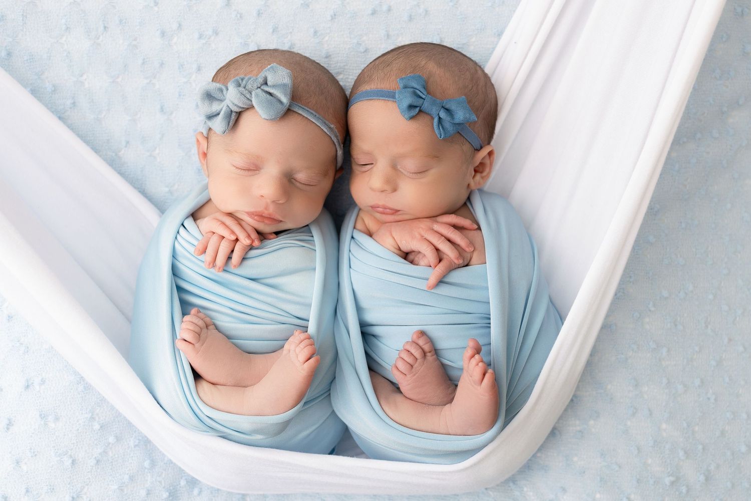 Five connected photos show newborn twins in matching light blue outfits and bows laying on white blankets.