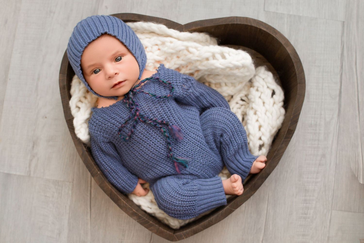 A baby wearing a blue knit sweater lies on a plush white blanket in multiple poses.