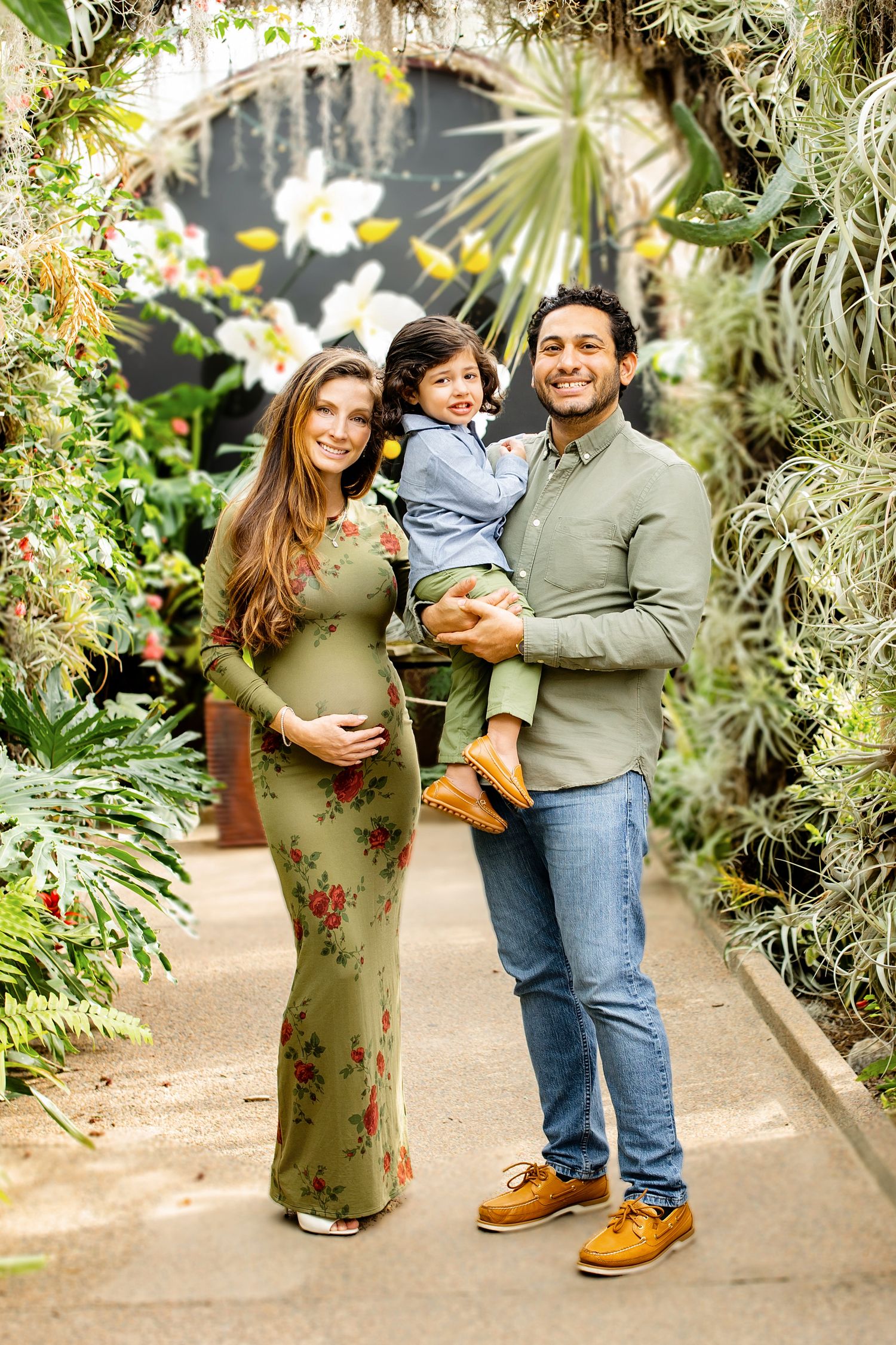 A couple poses together in a lush greenhouse setting with tropical plants and hanging air plants surrounding them.