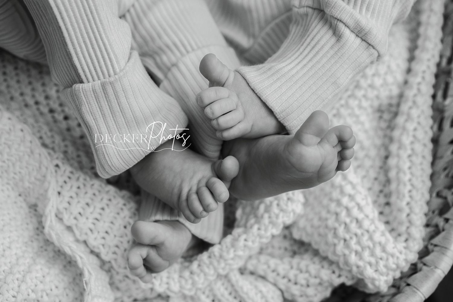 Black and white newborn photo of tiny baby feet resting on a soft knit blanket.