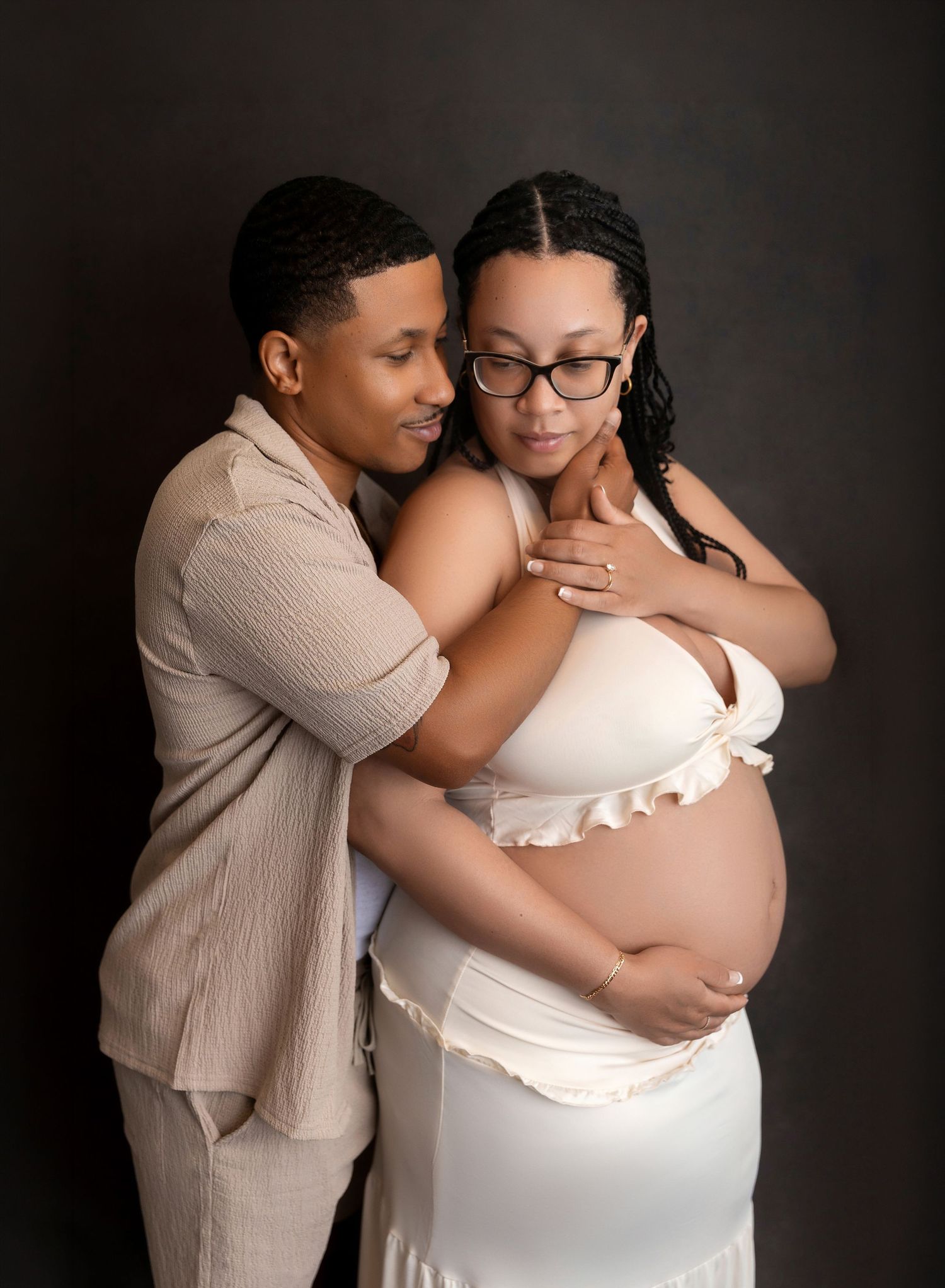 Couple embracing tenderly, pregnant woman in white dress with partner behind her.