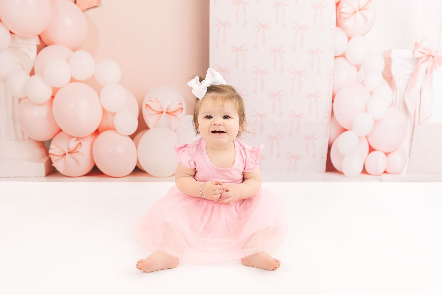 Pink balloons create a dreamy backdrop for a baby sitting on the floor in a tutu dress and headband.