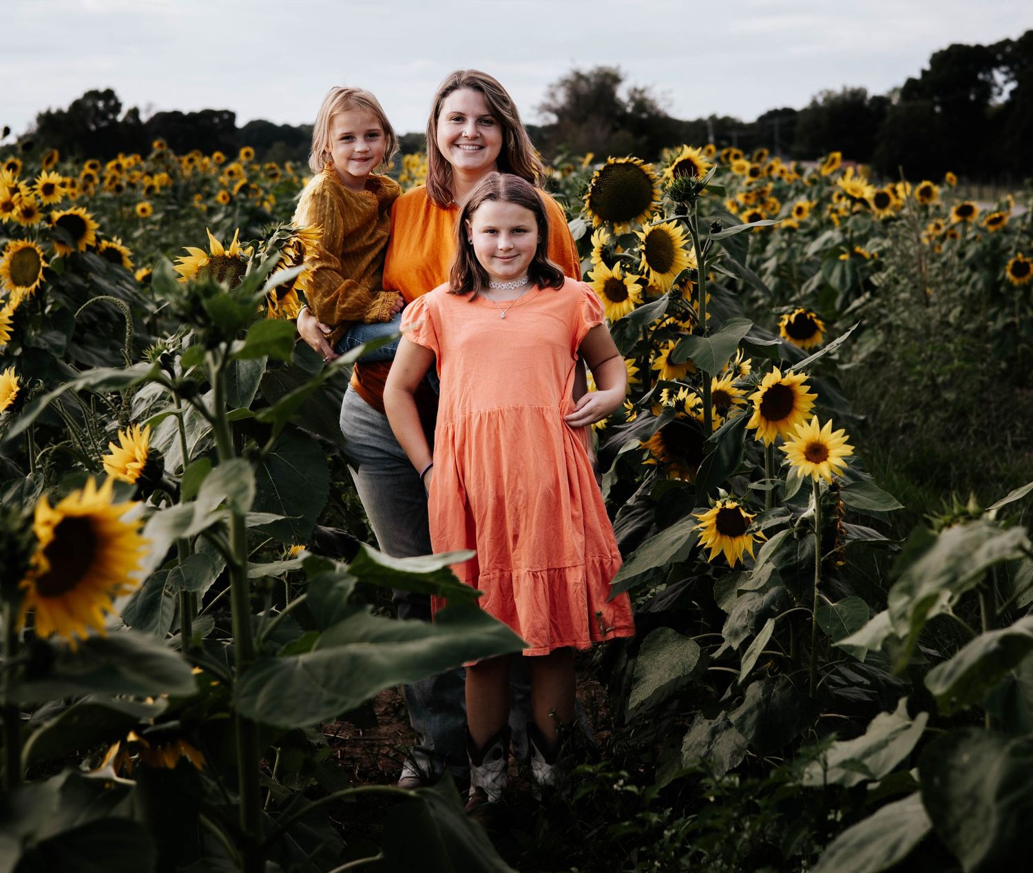 A bright orange dress stands out beautifully against a vibrant field of blooming sunflowers on a summer evening.
