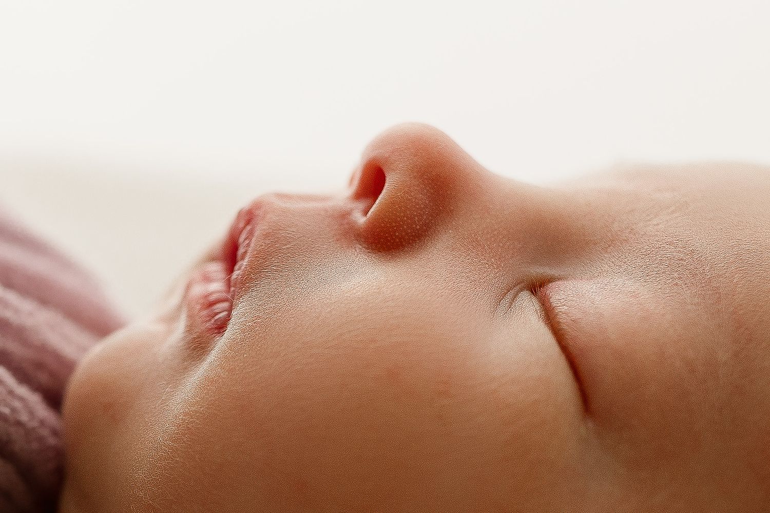 Close-up profile view of sleeping baby's face with soft pink blanket in background.