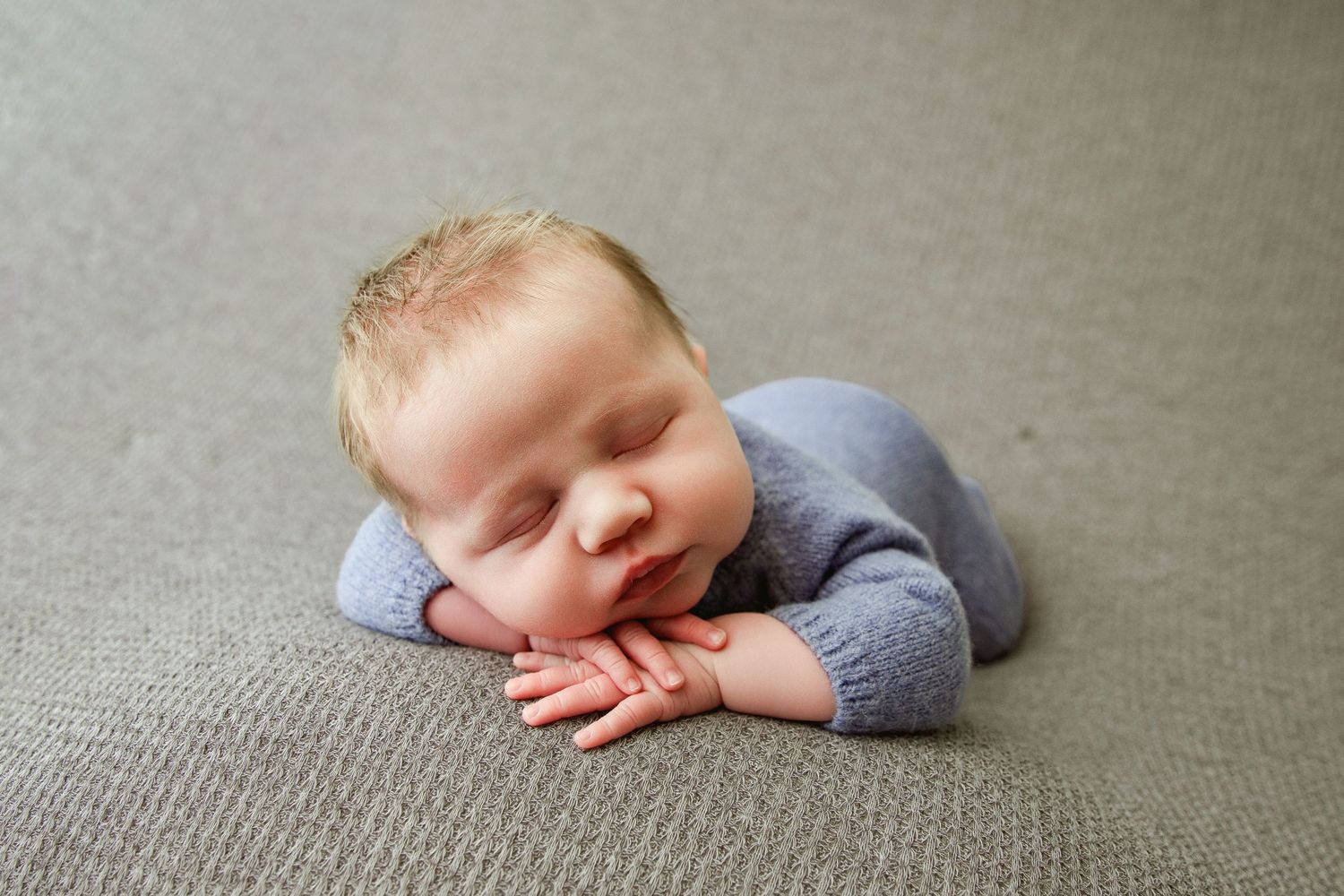 Newborn wearing grey outfit sleeping on grey carpet in studio setting.