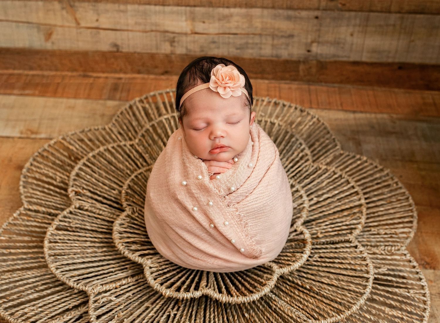 Sleeping newborn baby swaddled in pink wrap with floral headband in woven basket newborn photography.