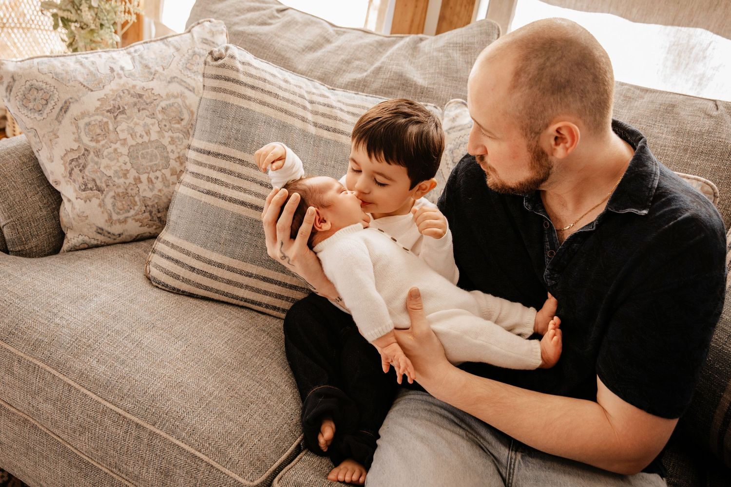 A heartwarming moment shared between two people sitting on a gray couch with decorative pillows in a sunlit room.