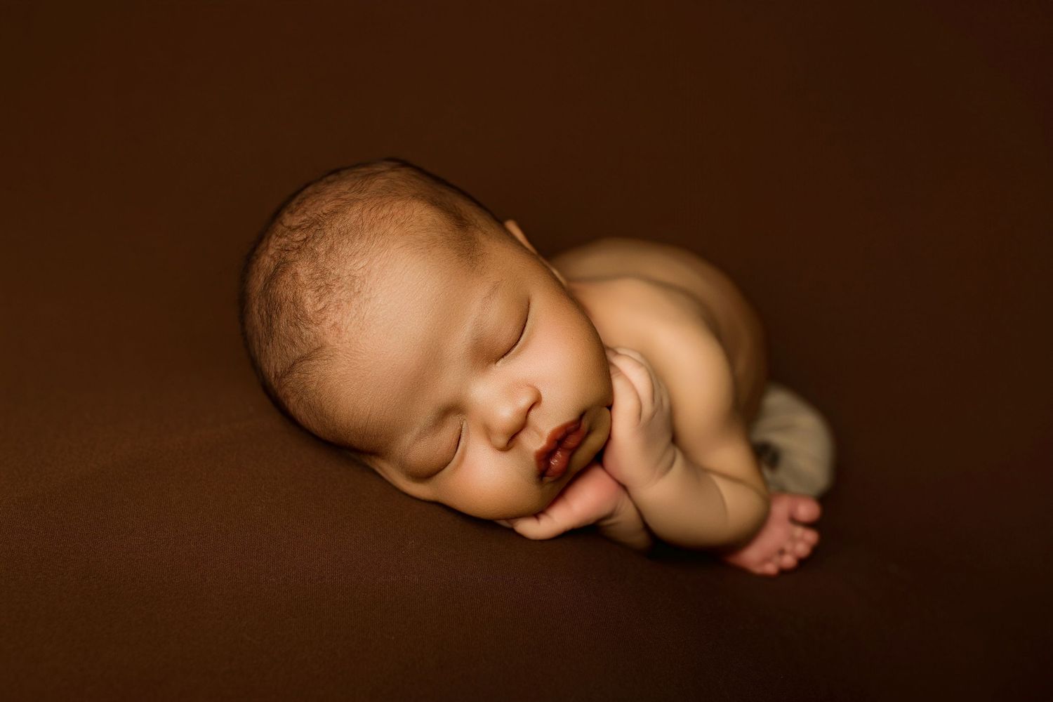 A collection of artistic sepia-toned baby portraits showing different poses and angles against a dark background.