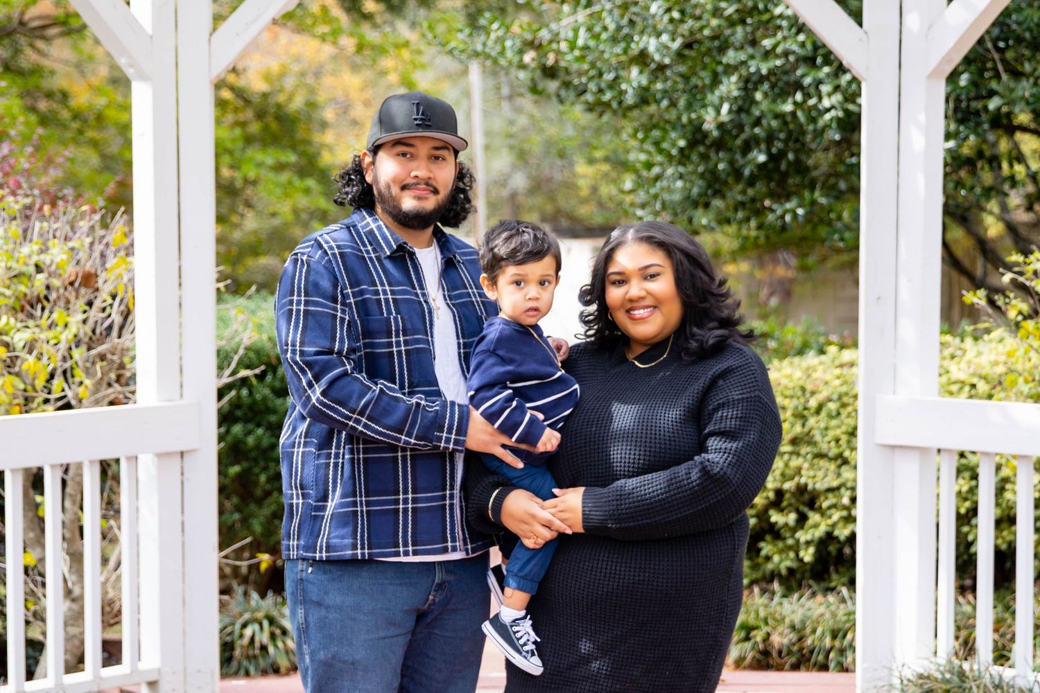 Family wearing coordinated blue and black outfits poses together in front of white gazebo during outdoor photo session.