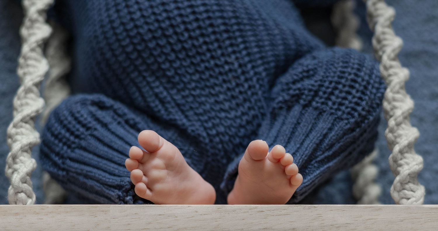 Small baby feet wearing a cozy knitted navy blue sock against a soft textured background.