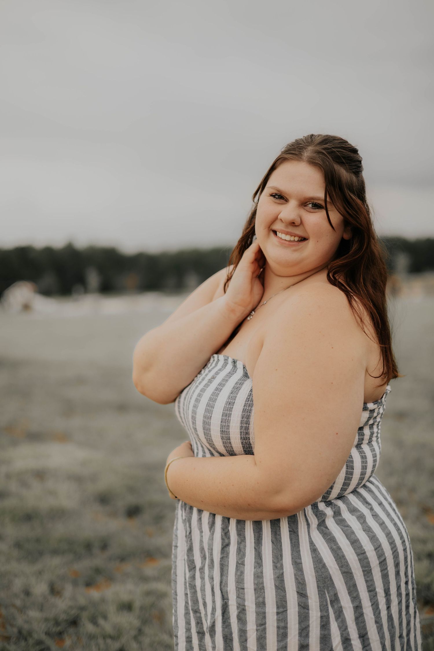 A series of outdoor portrait photos showing someone in a striped sundress posing on a cloudy beach.