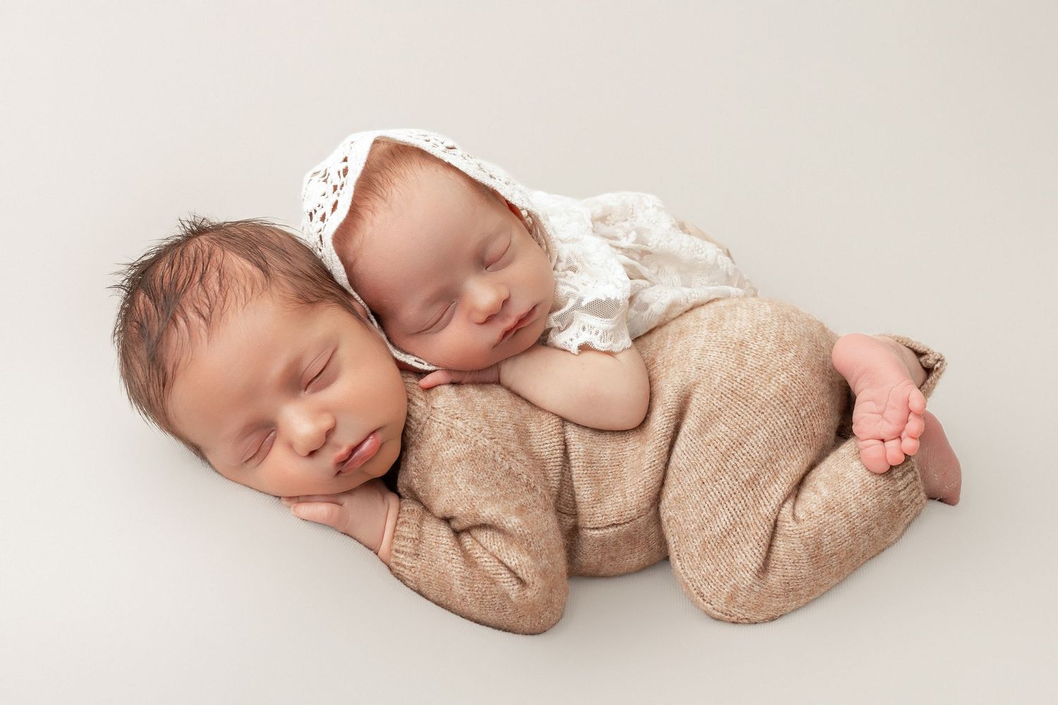 A sleeping baby wearing a soft beige knit outfit lies peacefully on a white backdrop.