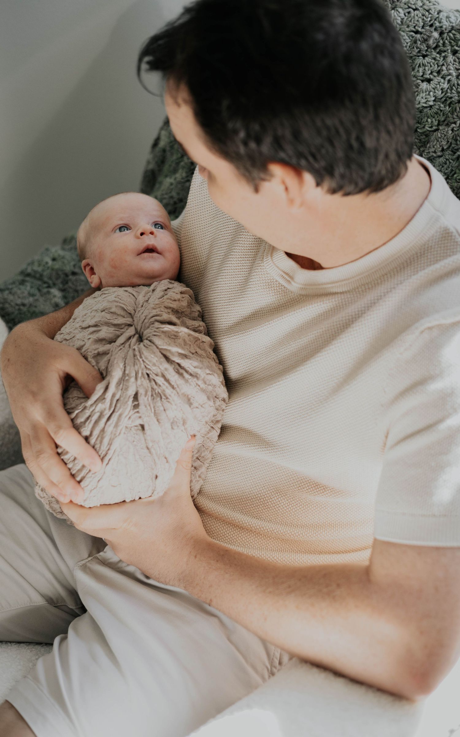 A series of intimate photos showing a parent holding and bonding with a newborn baby wrapped in beige cloth.