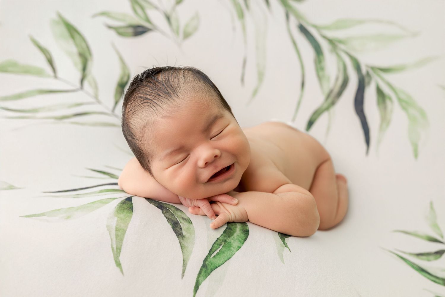 Smiling newborn baby sleeping peacefully on a white floral blanket with green leaves, perfect newborn photography pose.