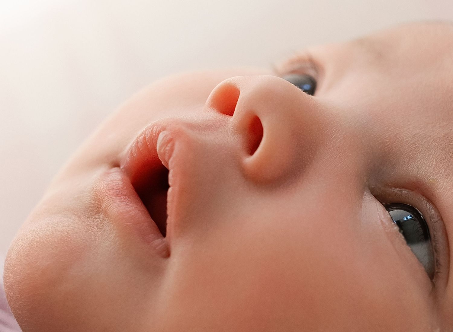 Close-up of a newborn baby face with blue eyes and tiny nose, soft skin detail photography.