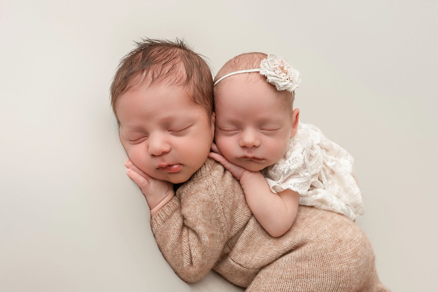Two sleeping newborn babies in beige swaddles lying together in peaceful slumber.