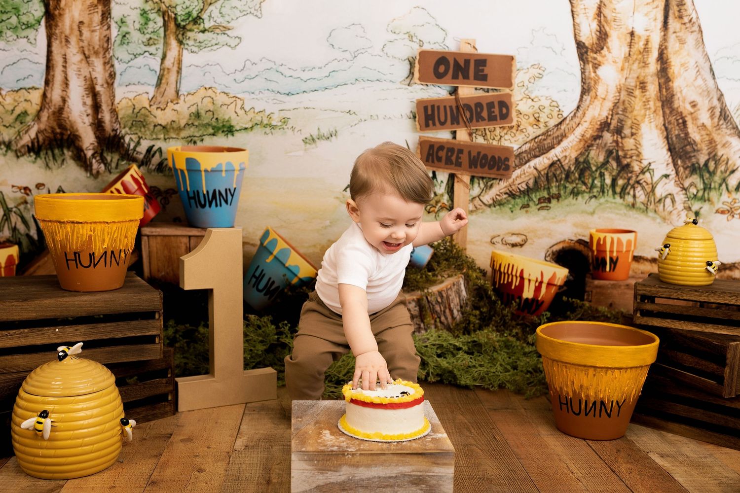A child's hands play with yellow honey-themed cake smash props during a first birthday photoshoot.