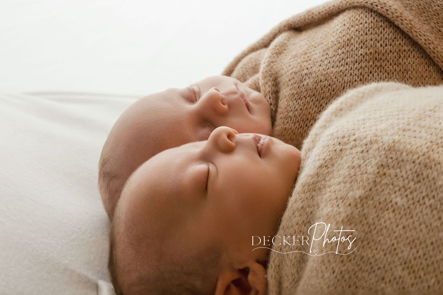 Two sleeping newborn twins wrapped in soft tan knit blankets, photographed by Decker Photos.