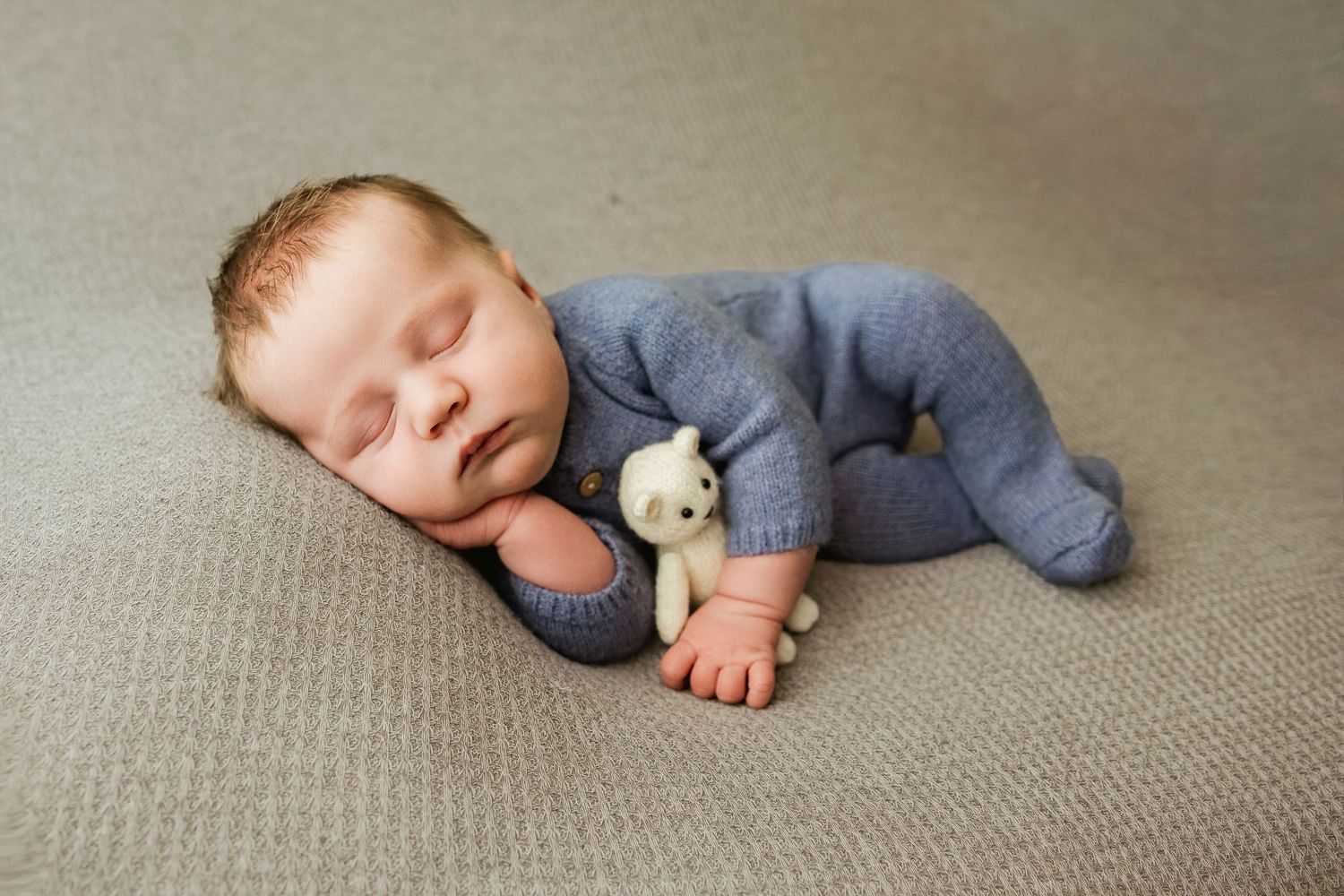A sleeping baby in a gray onesie lies peacefully on a textured beige carpet.