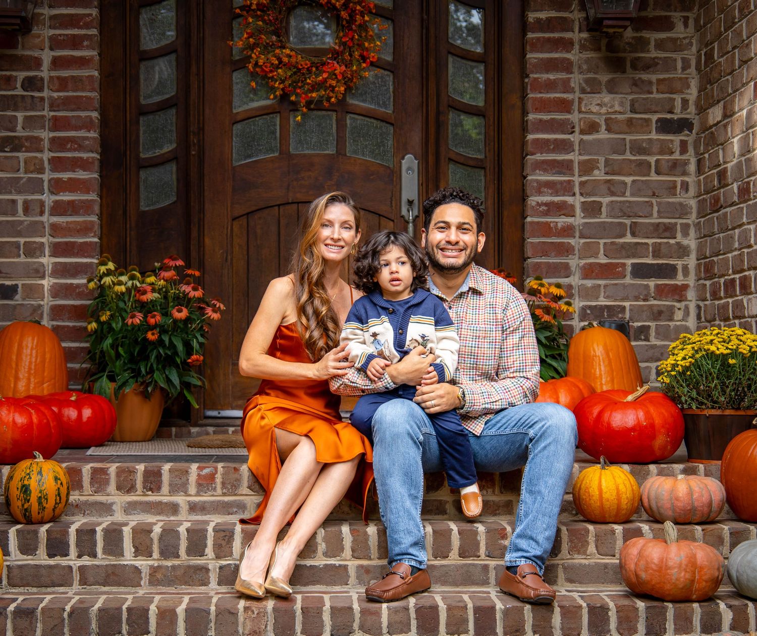 A couple sits on brick steps decorated with autumn pumpkins and fall decor for a seasonal photoshoot.