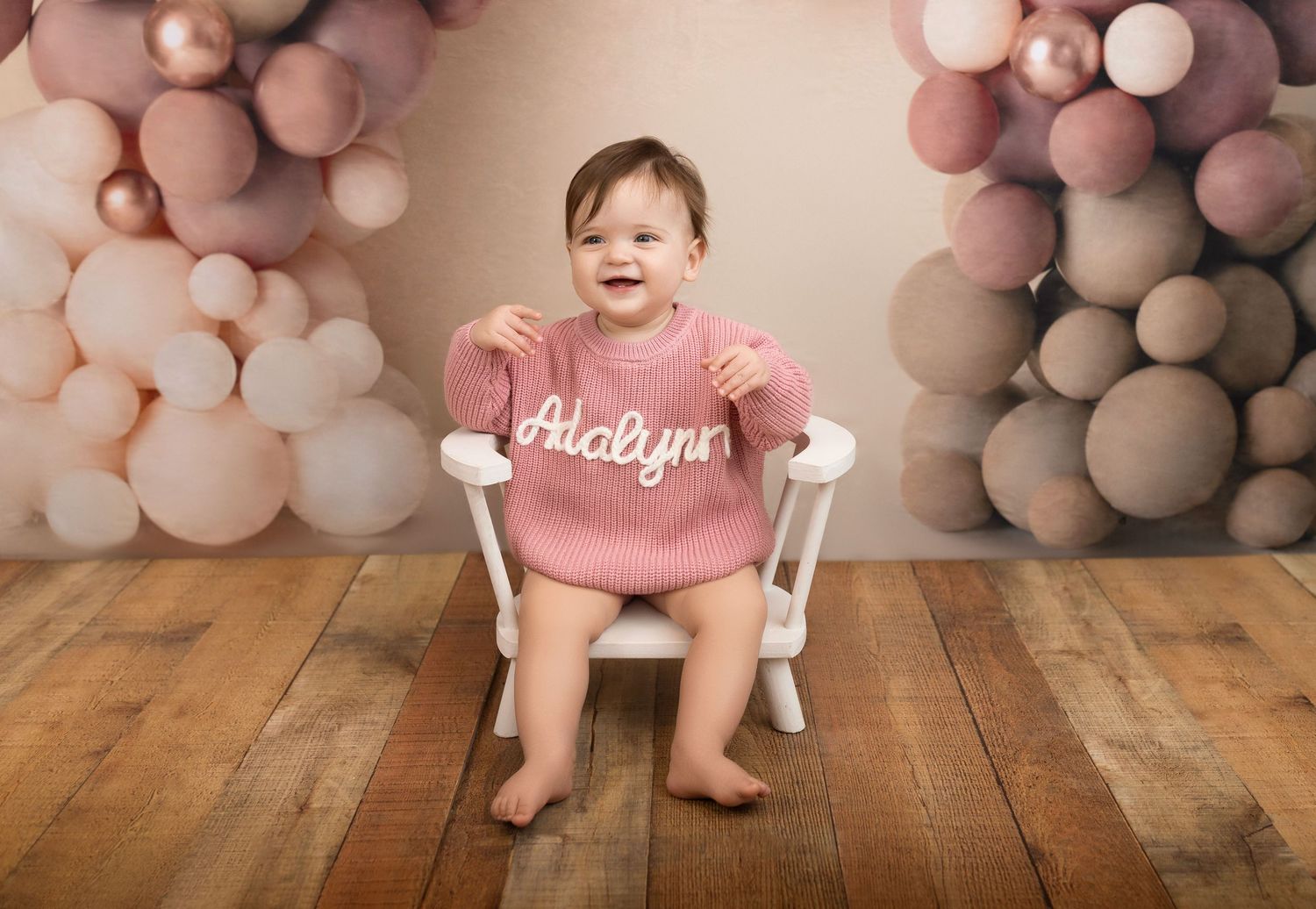 Festive pink and white balloon arch decorates a rustic wooden floor setting for a special celebration.