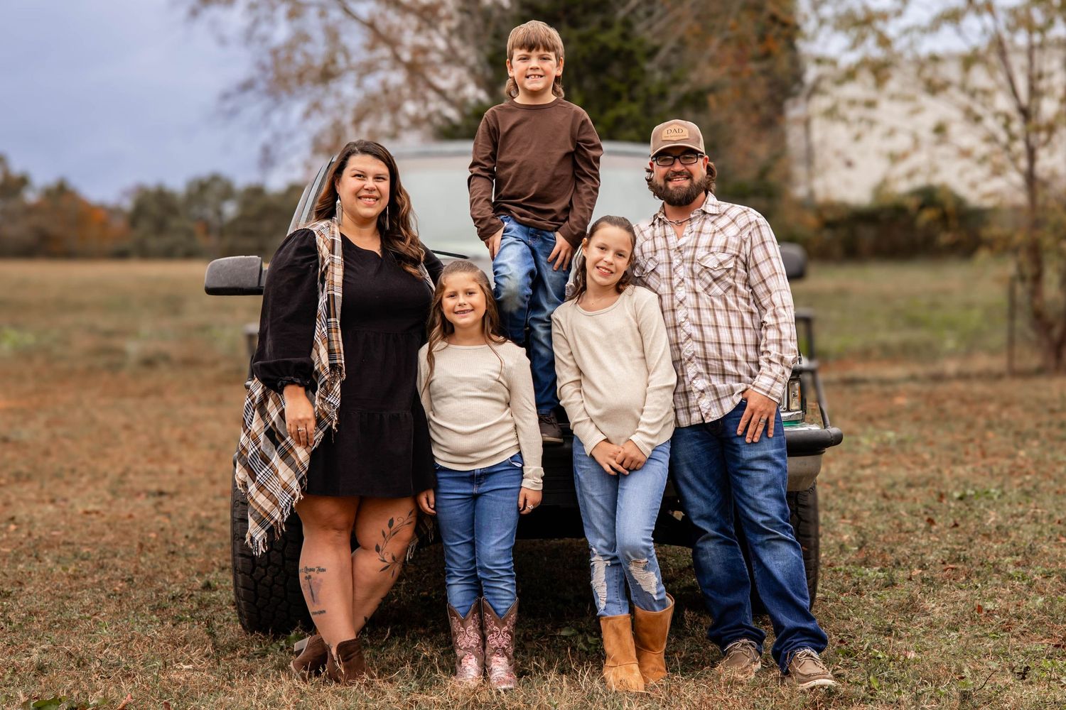 A group of people wearing casual clothing pose together outdoors in an autumn field during a family photoshoot.